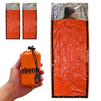 Orange emergency sleeping bag with reflective interior and compact storage pouch.
