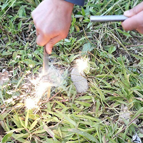 Person striking flint to start a fire on grass.