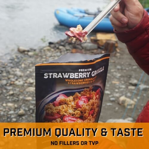 Person holding strawberry granola bag by a riverside.